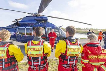 Im Vordergrund vier Einsatzkräfte in rot-gelber Kleidung, im Hintergrund blauer Hubschrauber