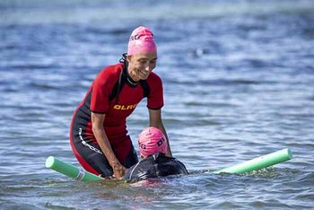 Kind auf Schwimmnudel im Meer mit Unterstützung Ausbilderin