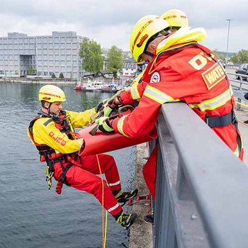 Mehrere Personen in rot-gelber Einsatzkleidung von beiden Seiten an Brückengeländer